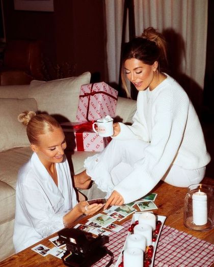 Two friends looking at polaroids beside wrapped gifts and candles