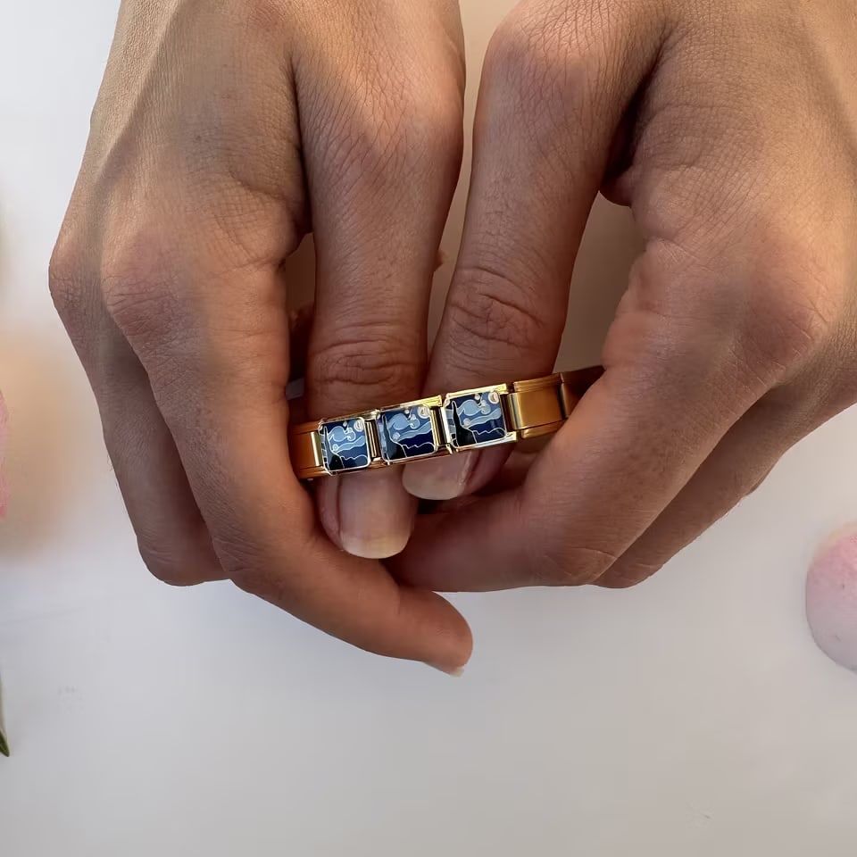 Aesthetically arranged display of Italian charm bracelet links alongside a closed book and a woman's hand
