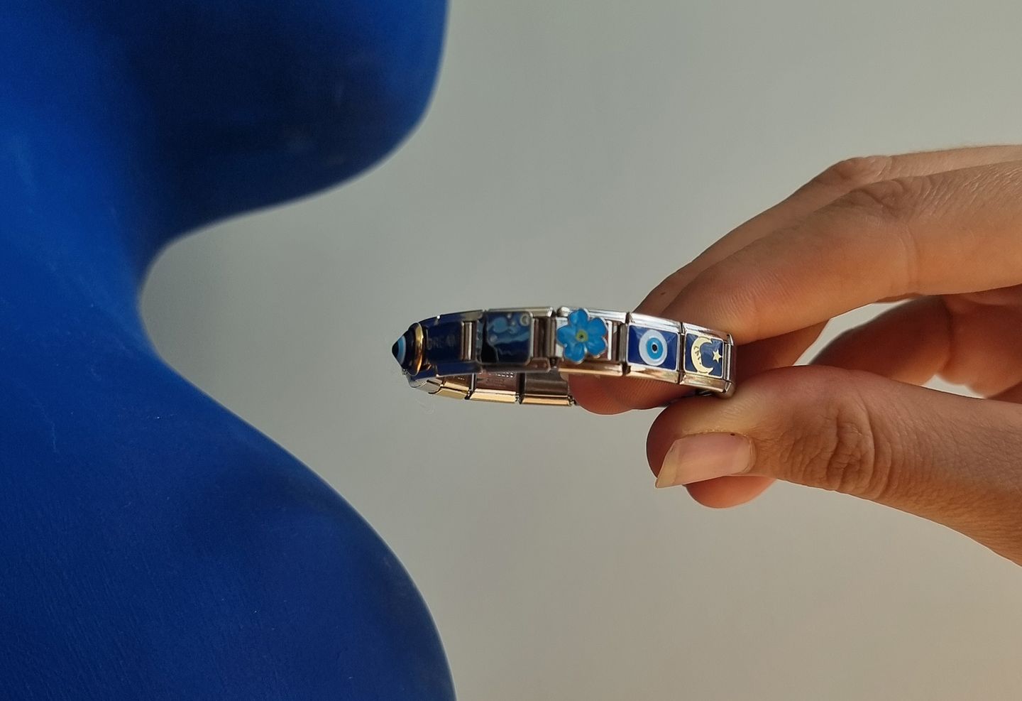 Italian charm bracelet with charms being hold by women hand next to blue statue