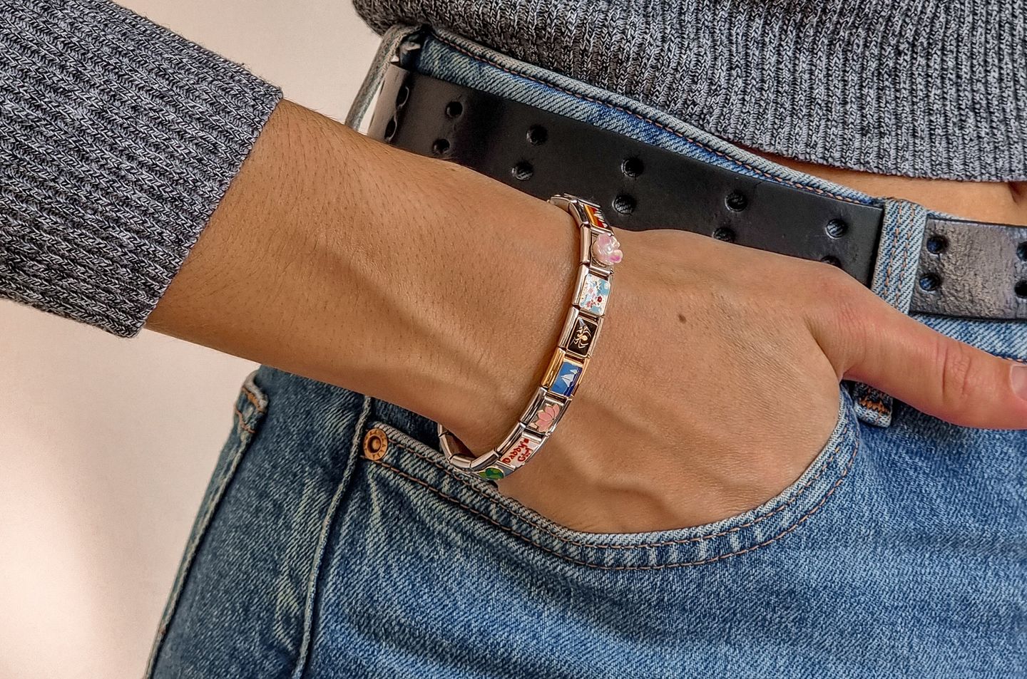 Women wearing italian charm bracelet with hand on pocket of blue jeans