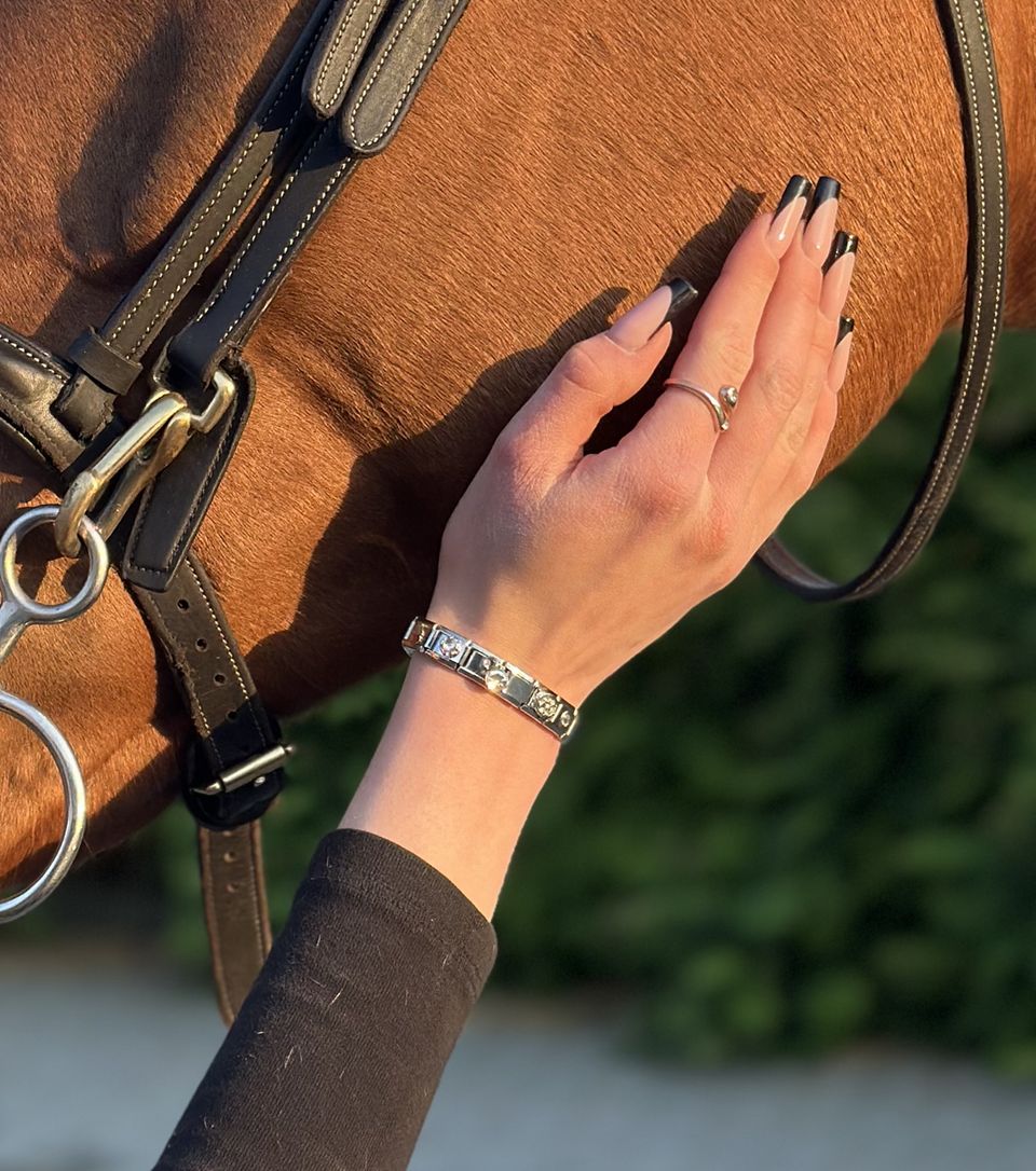 A woman's hand gently rests on a horse's side, showcasing a silver Italian charm bracelet
