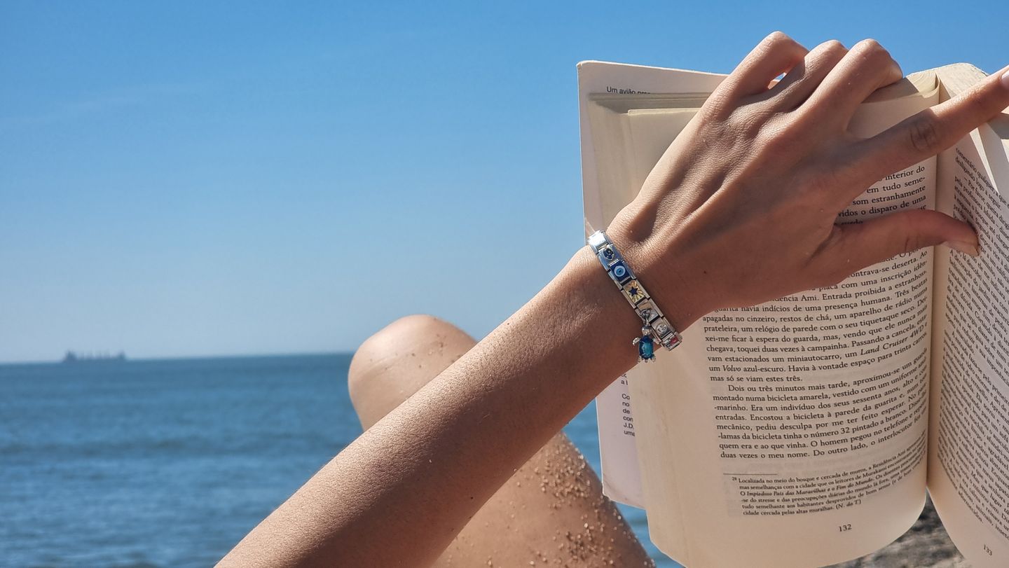 Aesthetically arranged display of Italian charm bracelet links alongside a closed book and a woman's hand